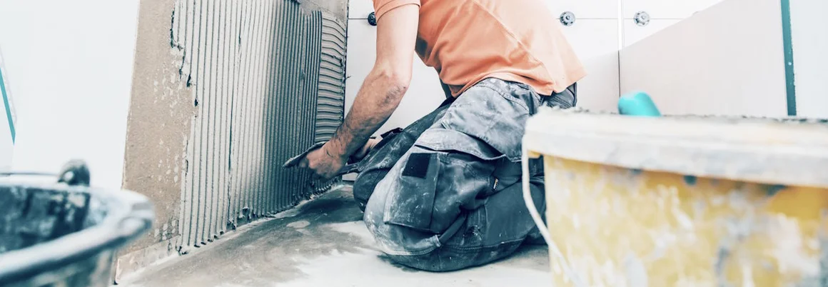 Person bringt Fliesenkleber mit Kelle an Wand an